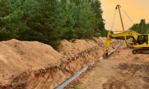 Excavator laying pipeline through forested terrain, highlighting the need for accurate boundary surveys in rugged land areas