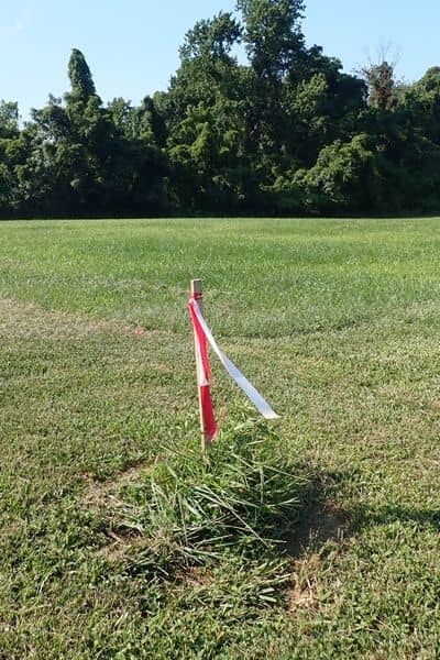  Boundary survey marker with red and white flag tape placed in a grassy field, marking property lines for accurate land measurement.

