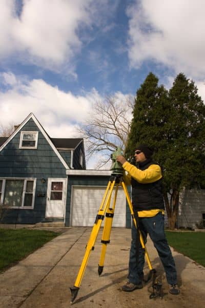 Land surveyor measuring flood elevation certificate - ALTA SURVEY Utah Licensed land surveyor using tripod equipment to measure home elevation for a flood elevation certificate