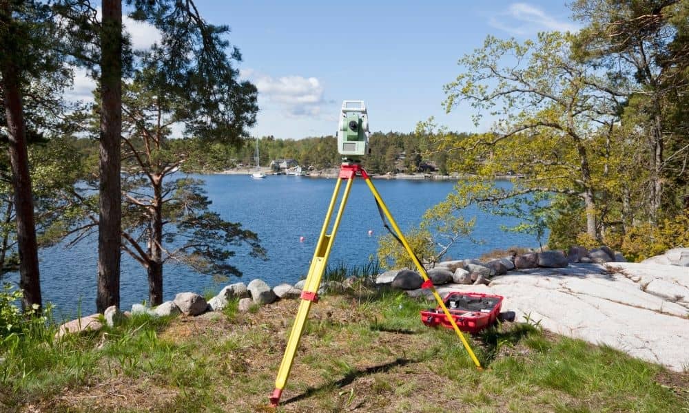 Boundary line survey lakefront property measurement - ALTA SURVEY Utah Total station set up on a tripod near a lake shoreline for a boundary line survey