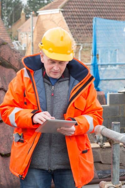 Boundary line surveyor reviewing data on tablet - ALTA SURVEY Utah Land surveyor in safety gear reviewing site data and maps on a digital tablet