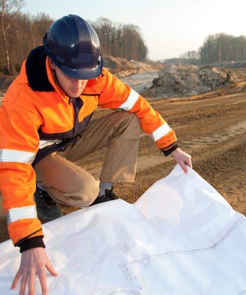Engineer reviewing road plans on-site to ensure accuracy during a construction survey