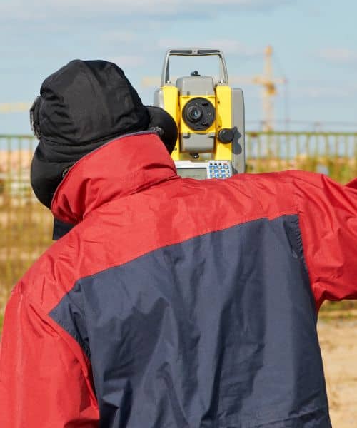 A land surveyor using a total station to mark accurate property boundaries during a property line survey