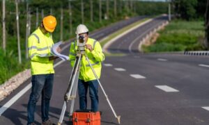 Survey crew reviewing road plans and taking elevation measurements as part of a construction survey for a roadway project