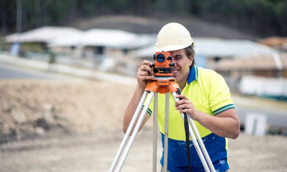 A licensed land surveyor using a total station to measure property at a construction site